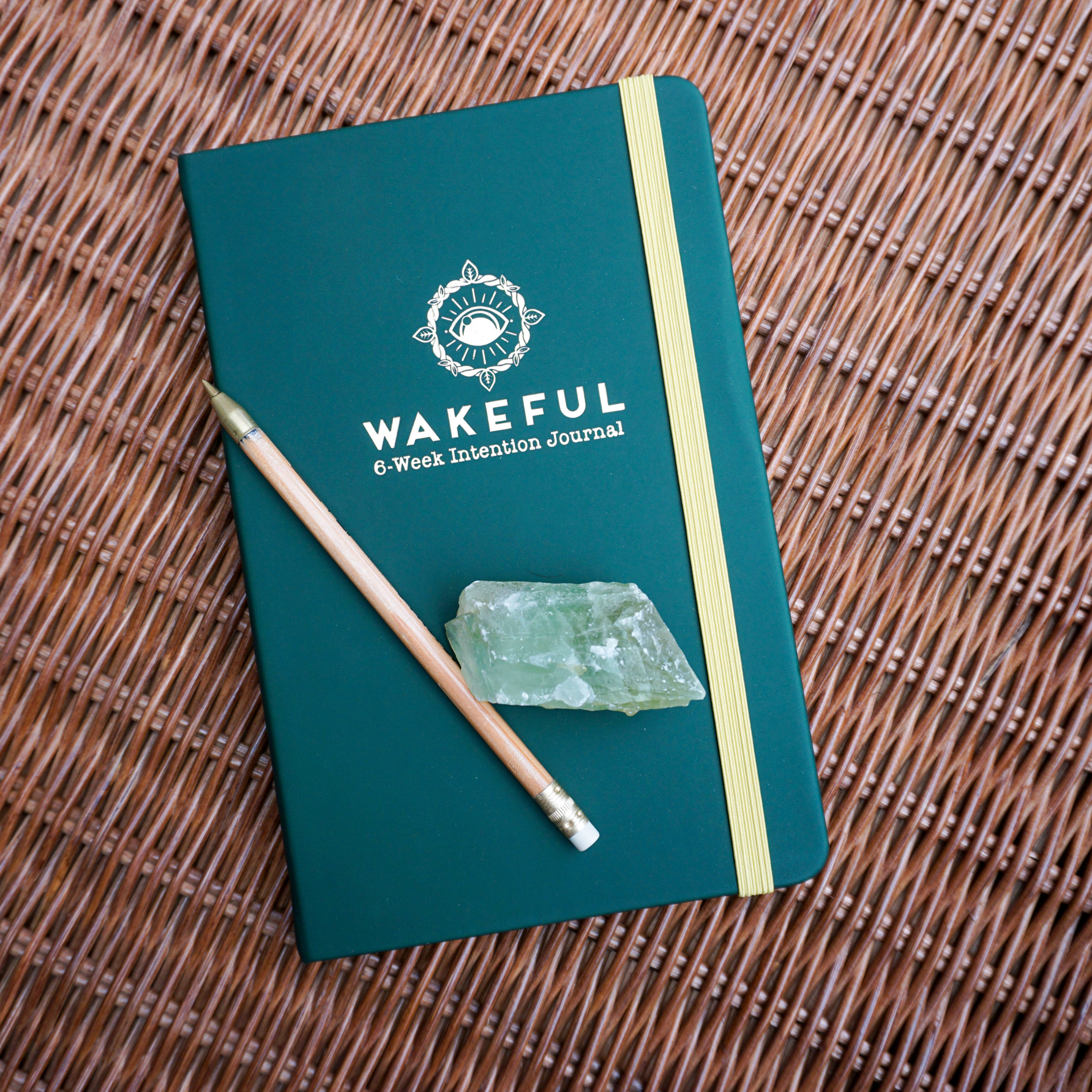 Wakeful Travel 6-week Microdosing Journal on brown rattan with a pencil and green crystal on it